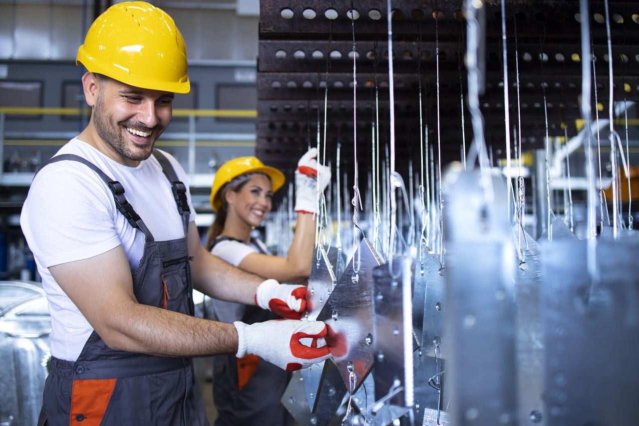 Factory employees with yellow hardhats inspecting metal parts in automobile factory.